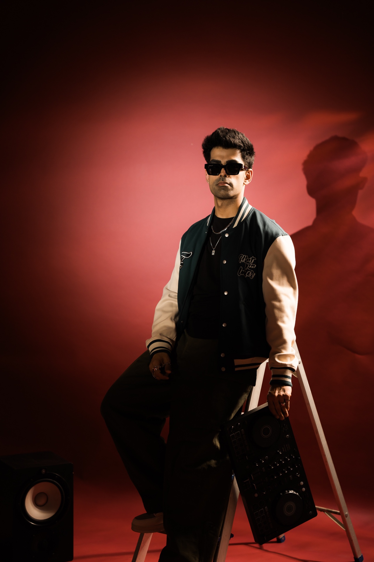 Bahul in a varsity jacket and shades against a deep red studio wash.
