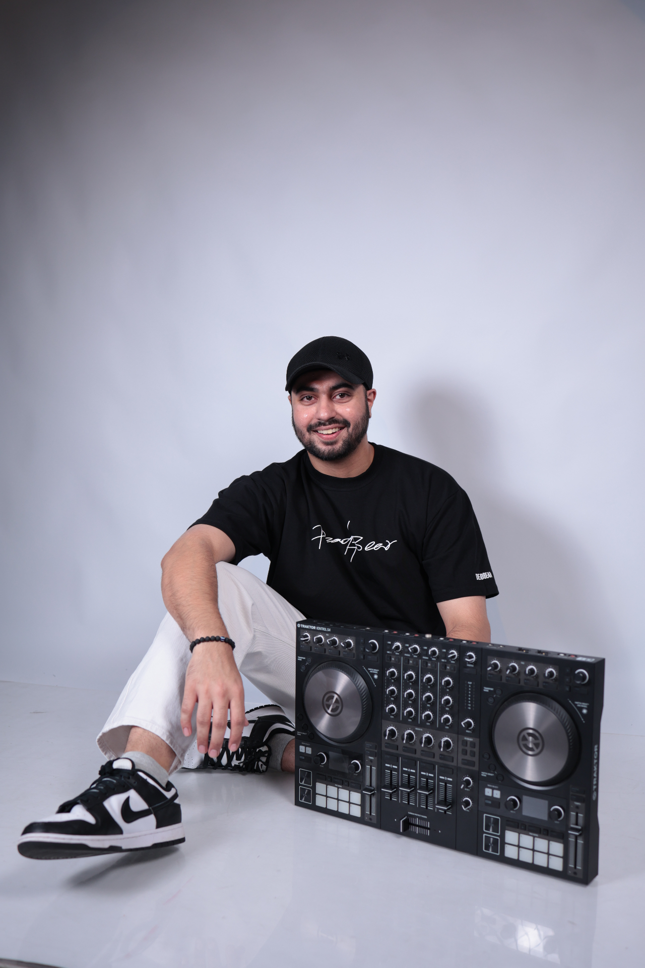 Sahib seated studio portrait in a black tee on a light backdrop.