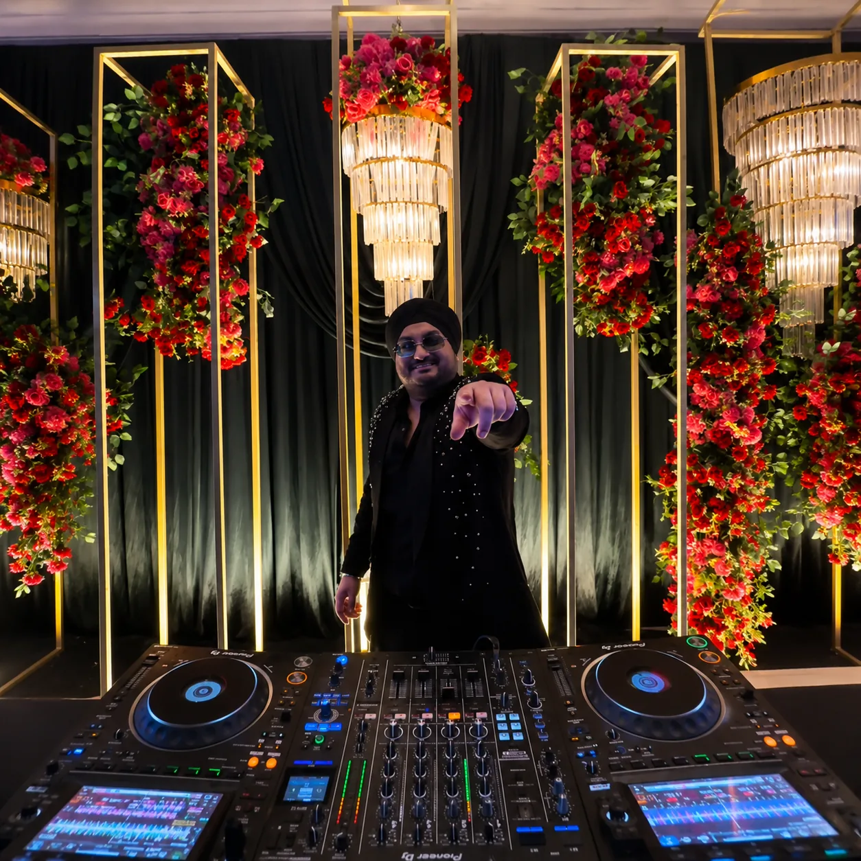 Tonu behind the decks at a luxury wedding, chandeliers and red florals framing the stage.