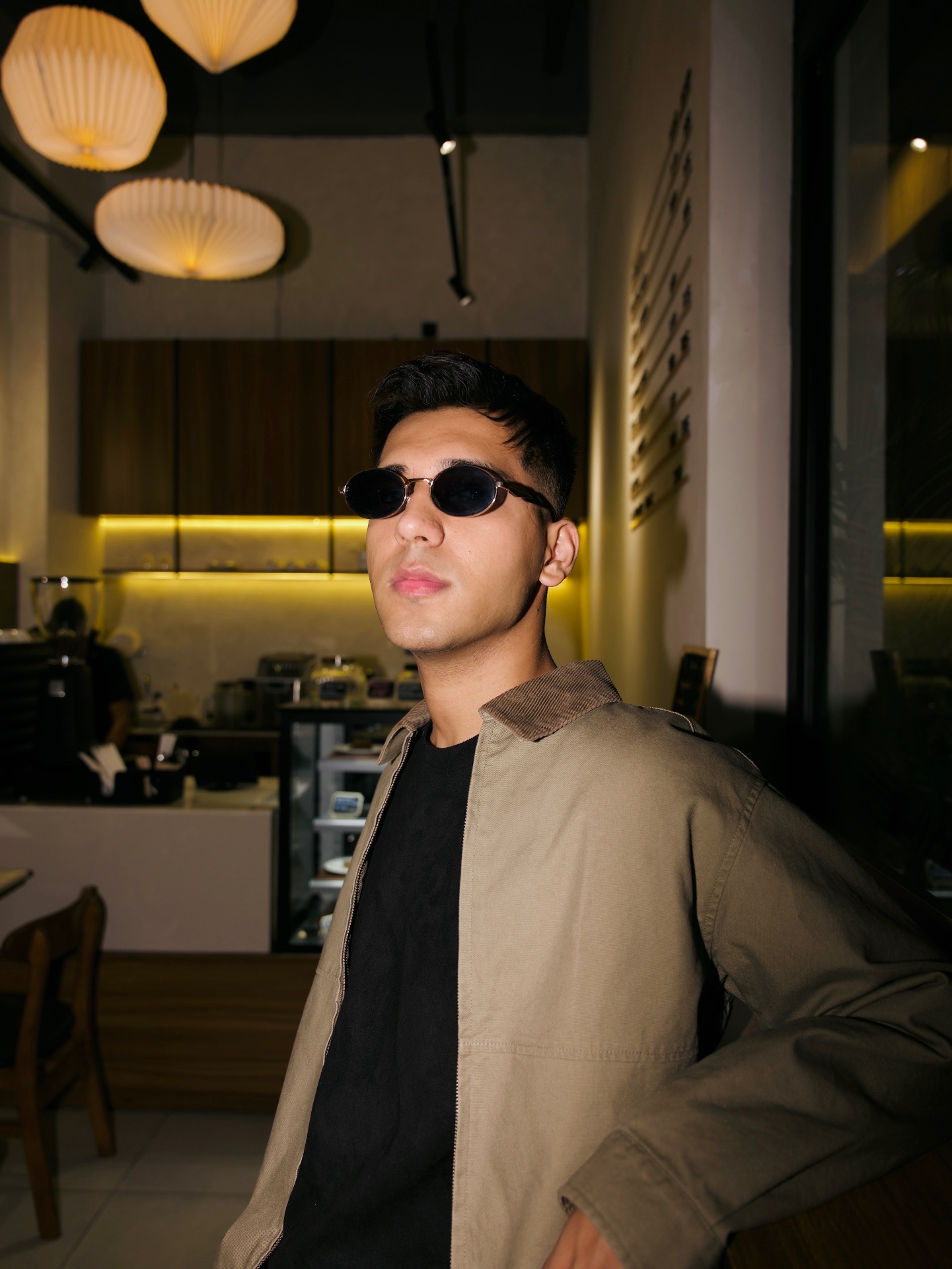 Exbow in shades and a khaki jacket inside a low-lit café.