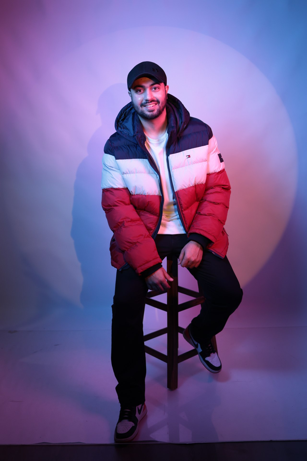 Sahib studio portrait on a stool under a warm halo backdrop.