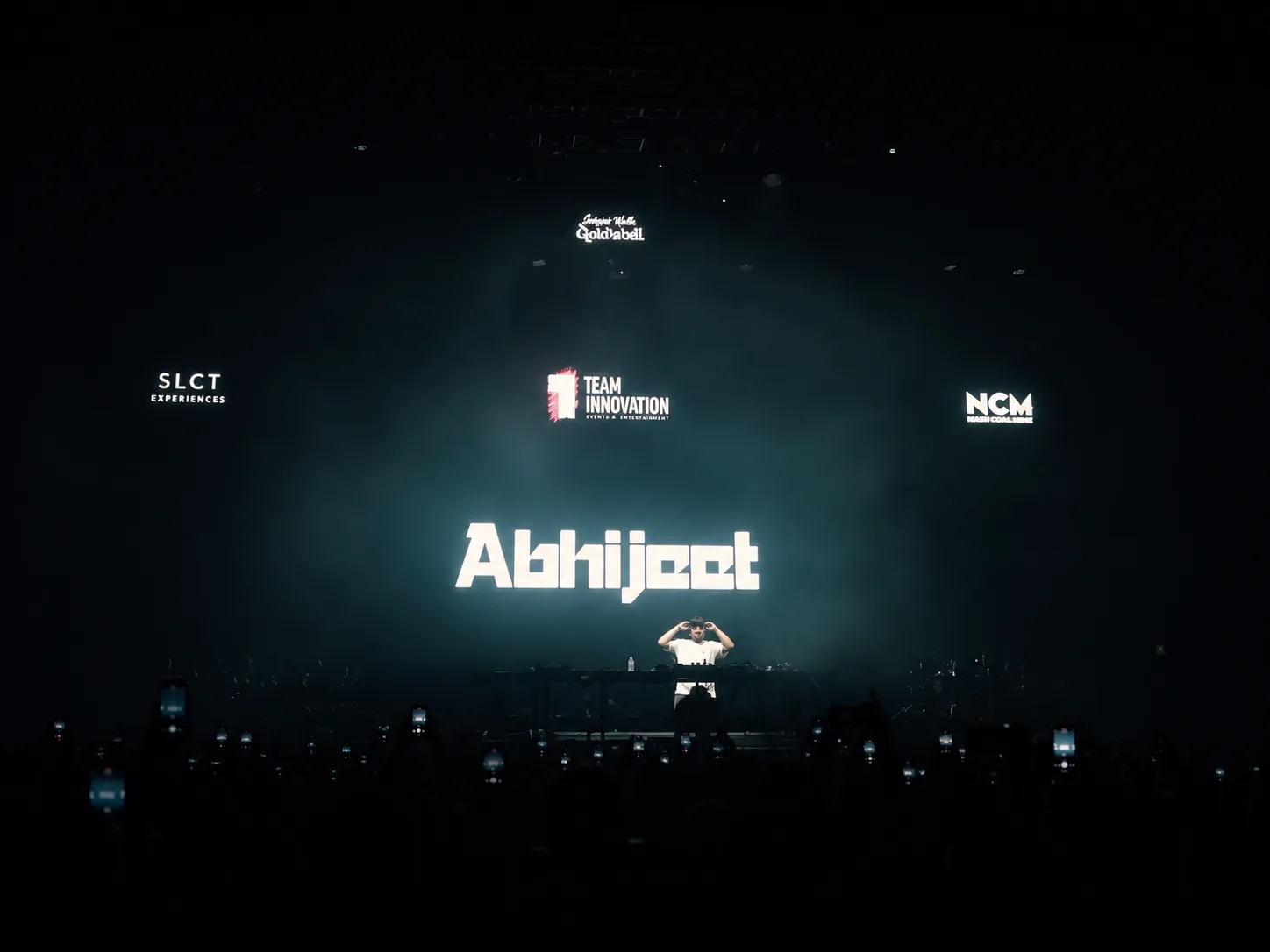 Tonu on stage with the SLCT Experiences × Abhijeet production, phones lit across the floor.