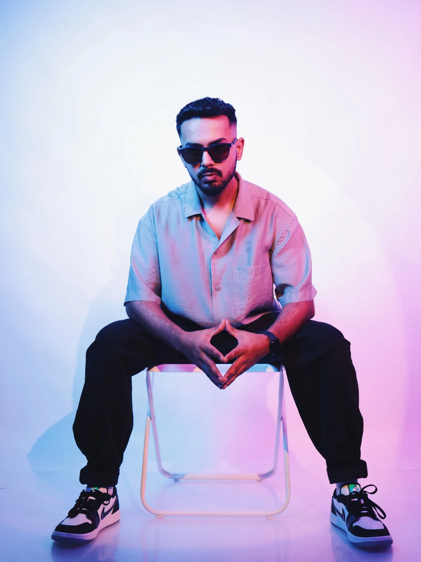 Max seated on a stool in a neon-lit pink and blue studio wash.