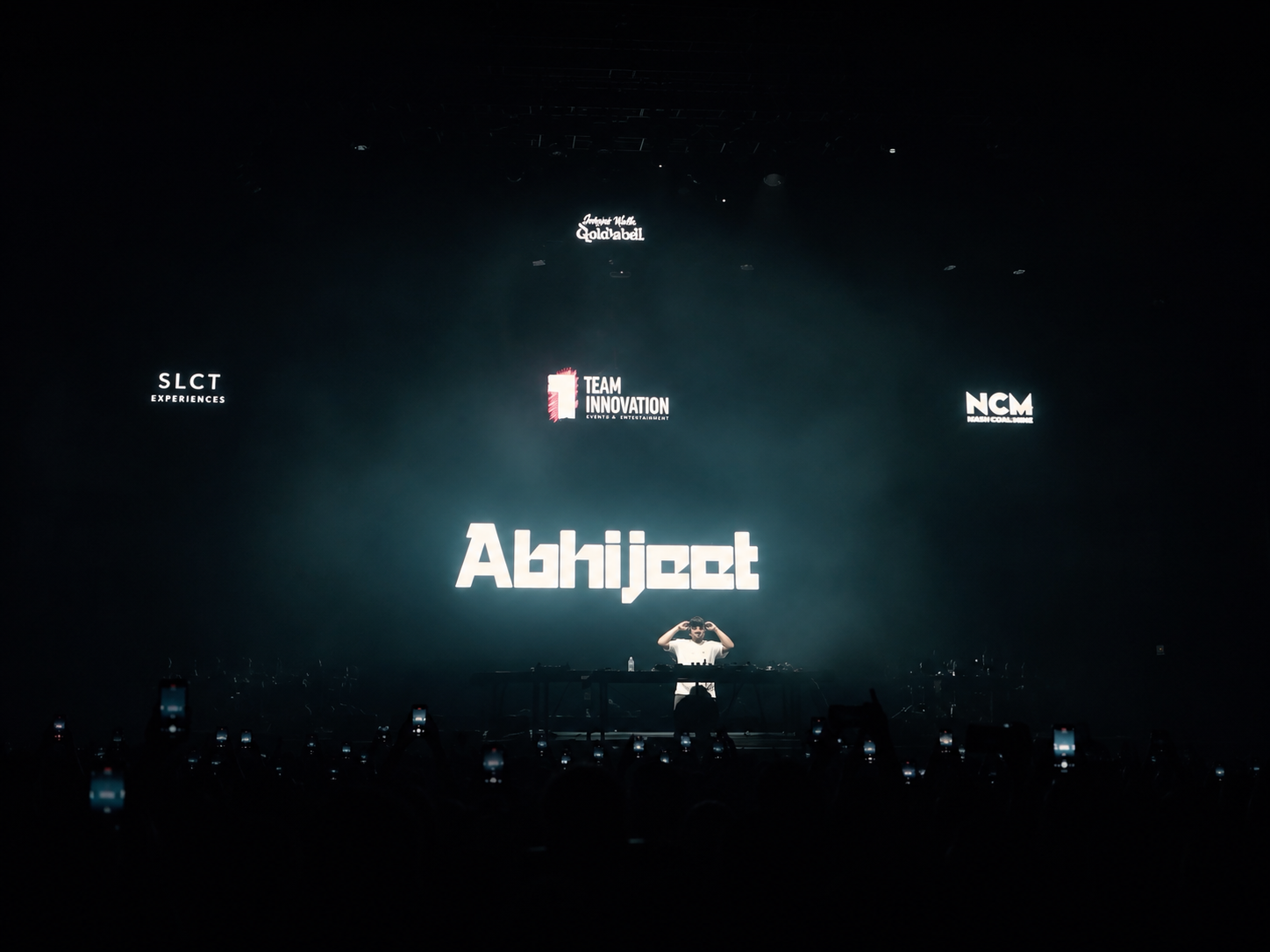 Tonu on stage with the SLCT Experiences × Abhijeet production, phones lit across the floor.