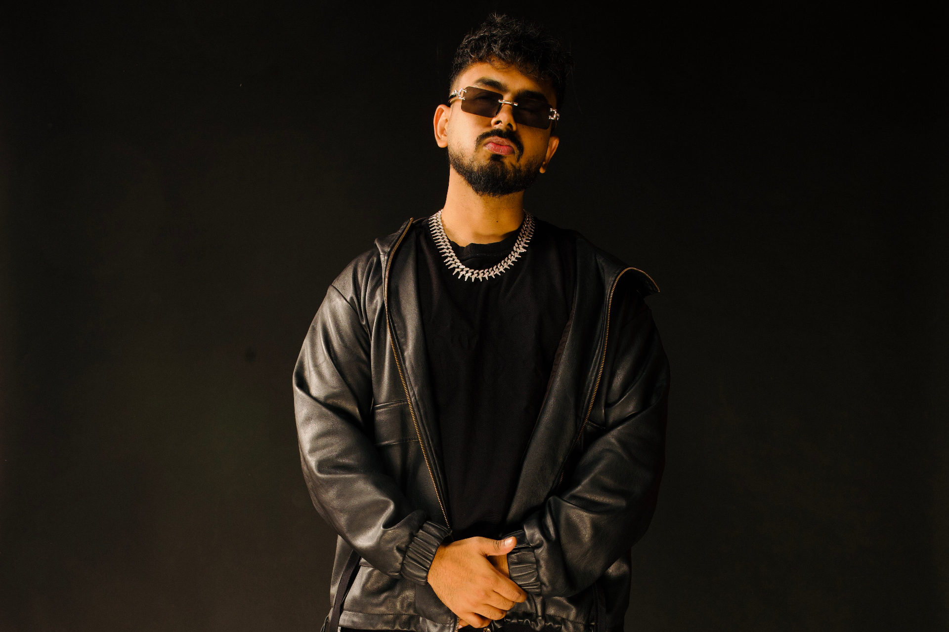 Max in a leather jacket and iced-out chain — editorial studio portrait.